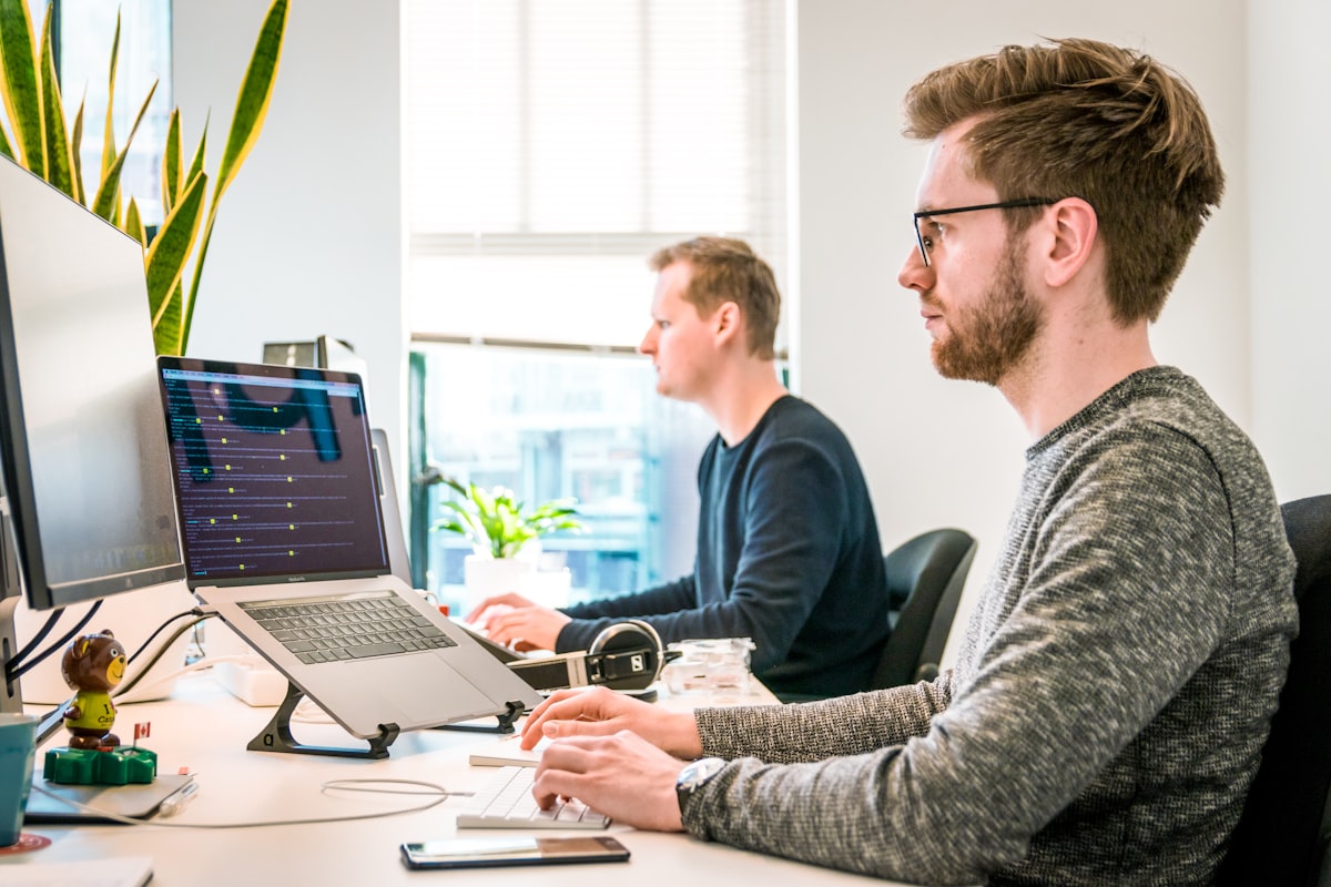 Two analysts working side by side at their laptops in a bright modern office, focused on data dashboards and predictive logistics models.