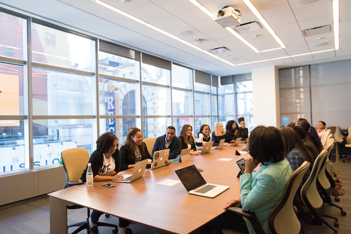 A diverse operations team seated around a long conference table with laptops open, reviewing dashboards in a bright modern office.